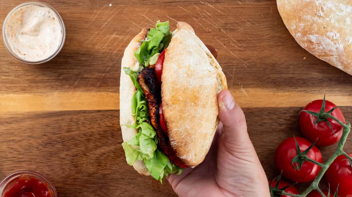A hand holding the burger sideways to show the fillings.