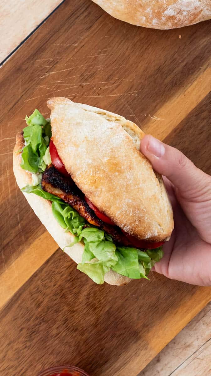 An angled view of a hand holding the Per Peri burger sideways to show the filling.