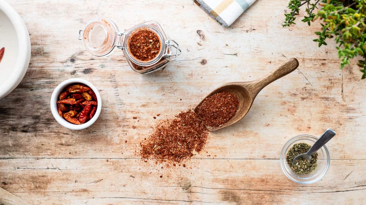 Overhead view of the Peri Peri seasoning spilling from a wooden scoop, surrounded by various seasoning ingredients.