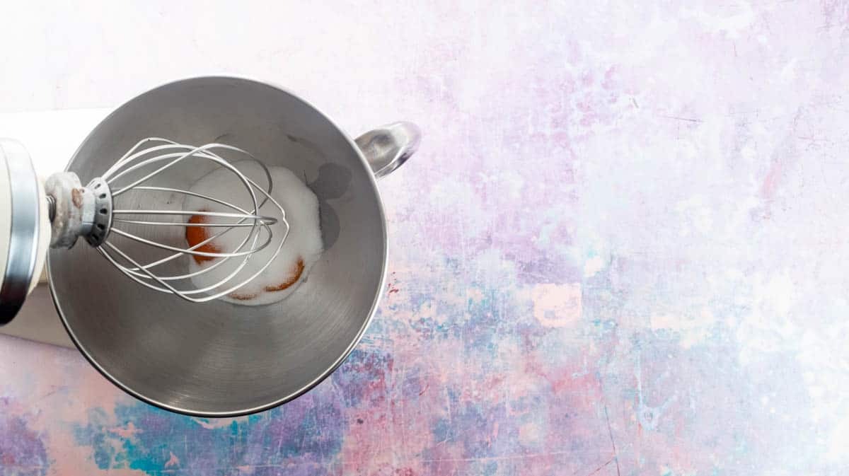 A stand mixer with the whisk attached. In the silver bowl there are egg yolks with caster sugar.