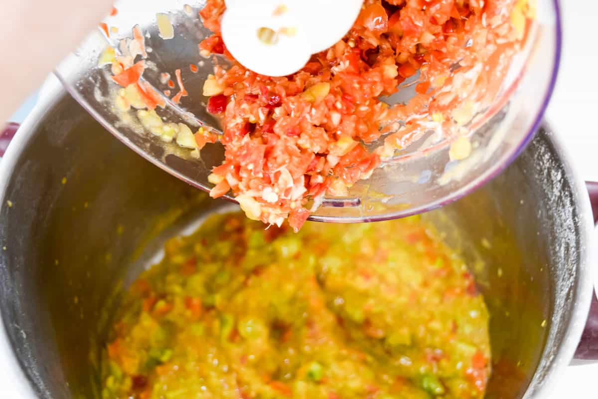 Chopped red pepper being poured in a large saucepan contained blended tomatoes.