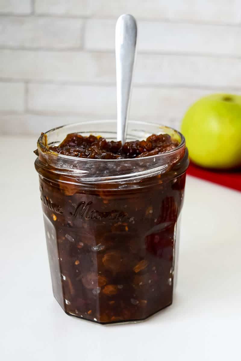 A front view of a glass jar filled with tomato and apple chutney.
