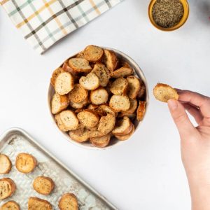 An overhead view of a bowl of bagel crisps with a hand holding one next to it.