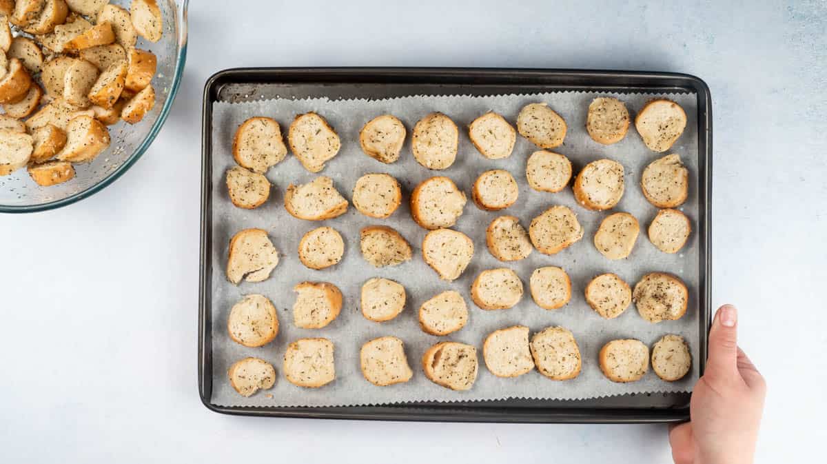 A lined baking tray with unbaked bagel chips laid out on top in a single layer.
