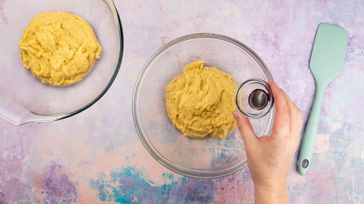 A hand is tipping pink food colouring into a bowl containing cake batter.