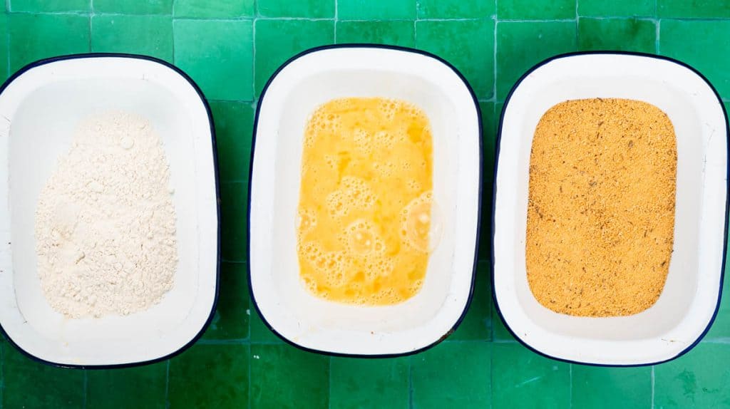 An overhead view of three bowls one containing flour, the next with beaten egg, and the final one with golden bread crumbs.