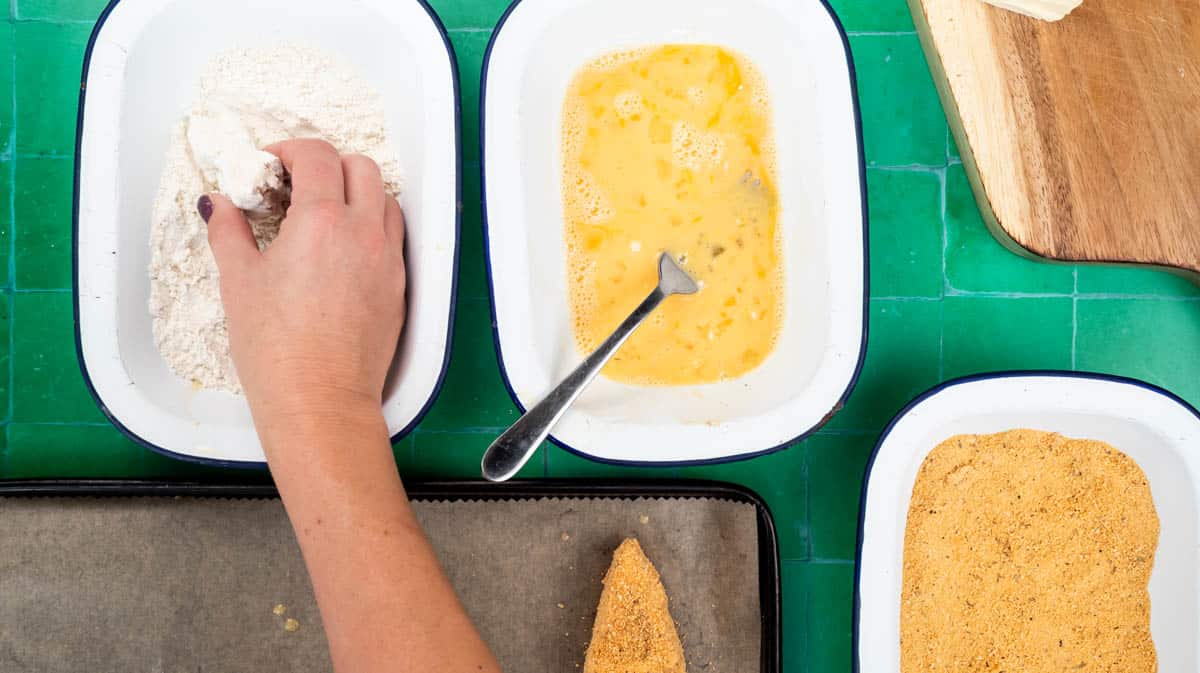 A hand is coating a camembert wedge in flour.