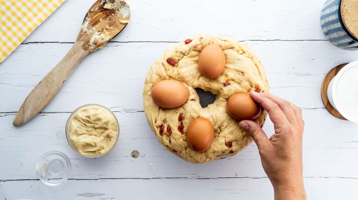 A hand is placing raw eggs on top of unbaked casatiello dough in a round bundt tin.