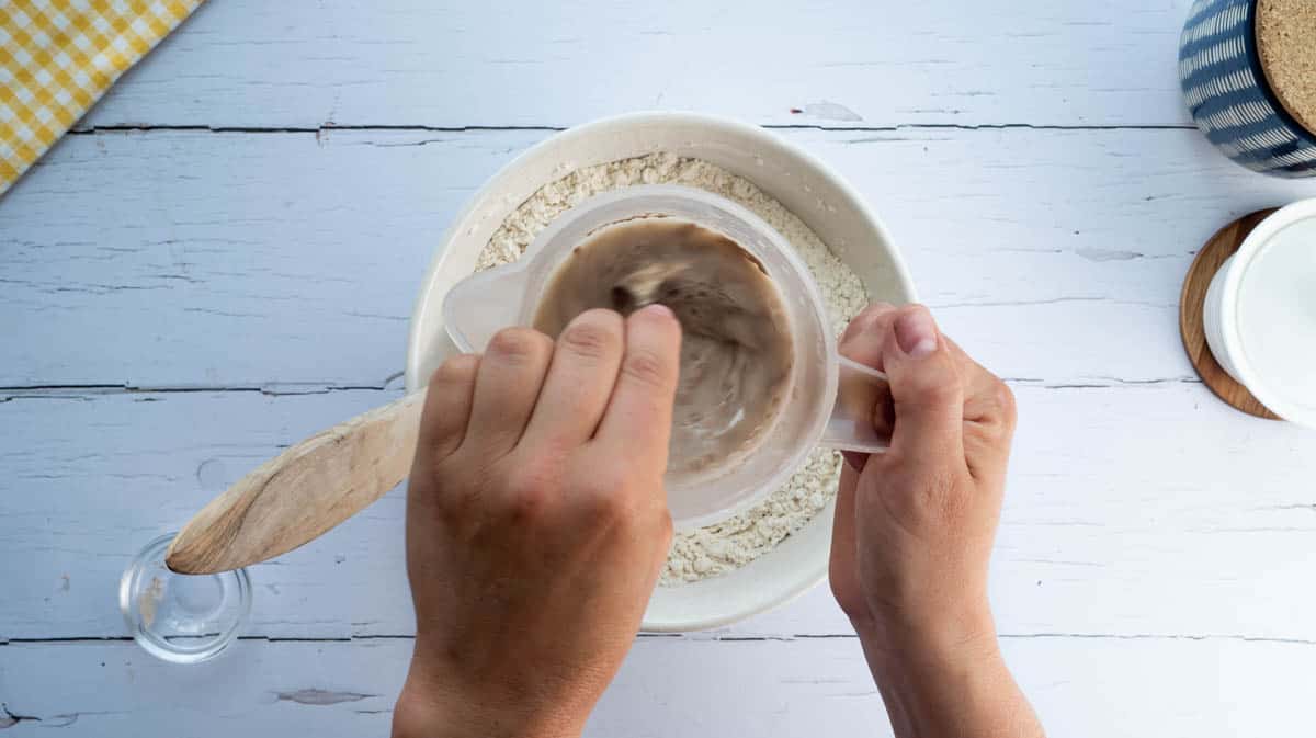 A hand is using a spoon to mix yeast and honey into water.