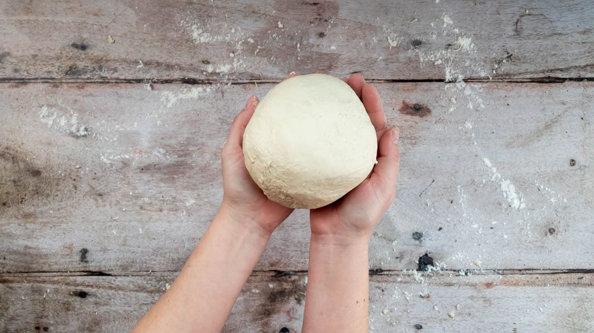 Two hands are cupping a ball of bread dough.