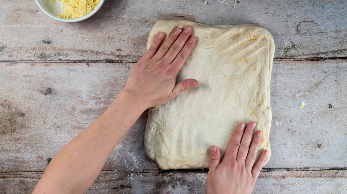 Two hands are pressing the bread dough into a rectangular shape ready to begin proofing.