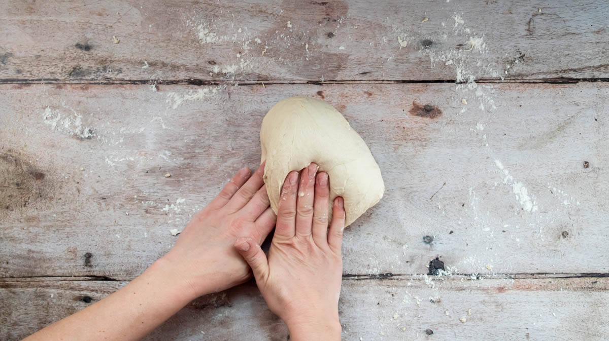 Two hands are finalising the kneading of the bread dough on a floured surface.