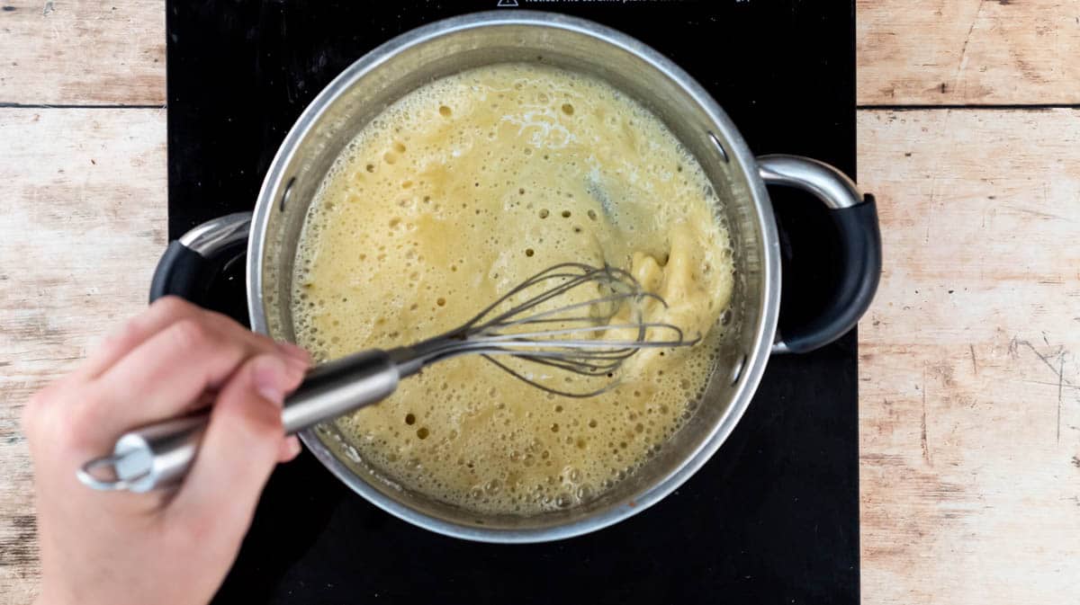 My hand is using a whisk to mix flour and butter together to make a roux.
