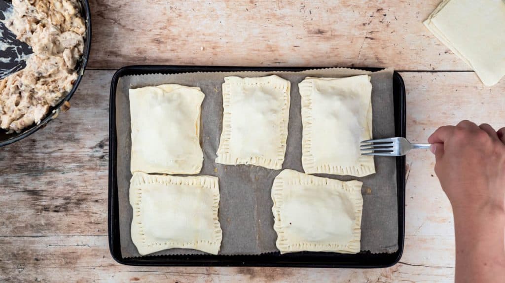 A hand is using a fork to crimp the edges of the puff pastry rectangles together to seal them.
