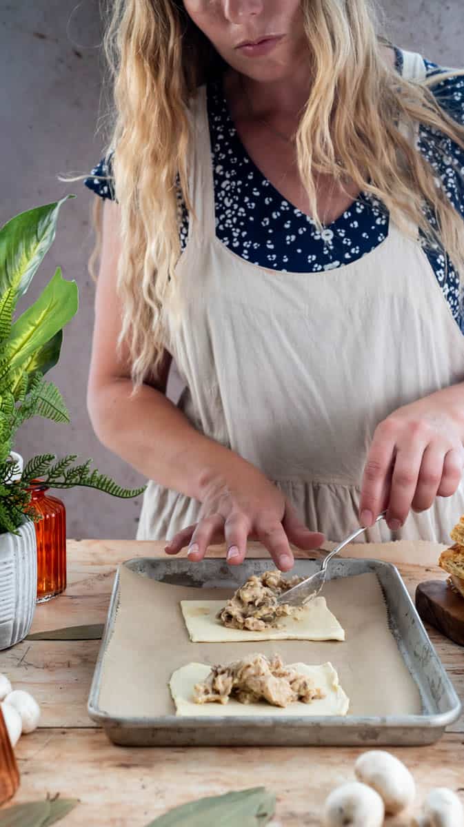 A person is spooning creamy chicken and mushroom filling onto a rectangle of puff pastry.