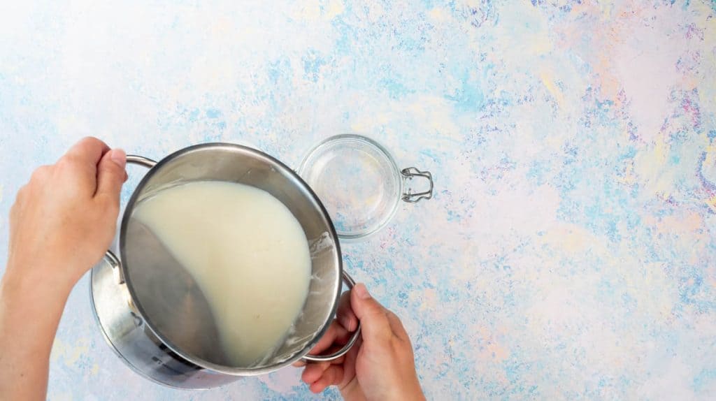 Two hands are pouring prepared condensed milk into a sterilised jar.