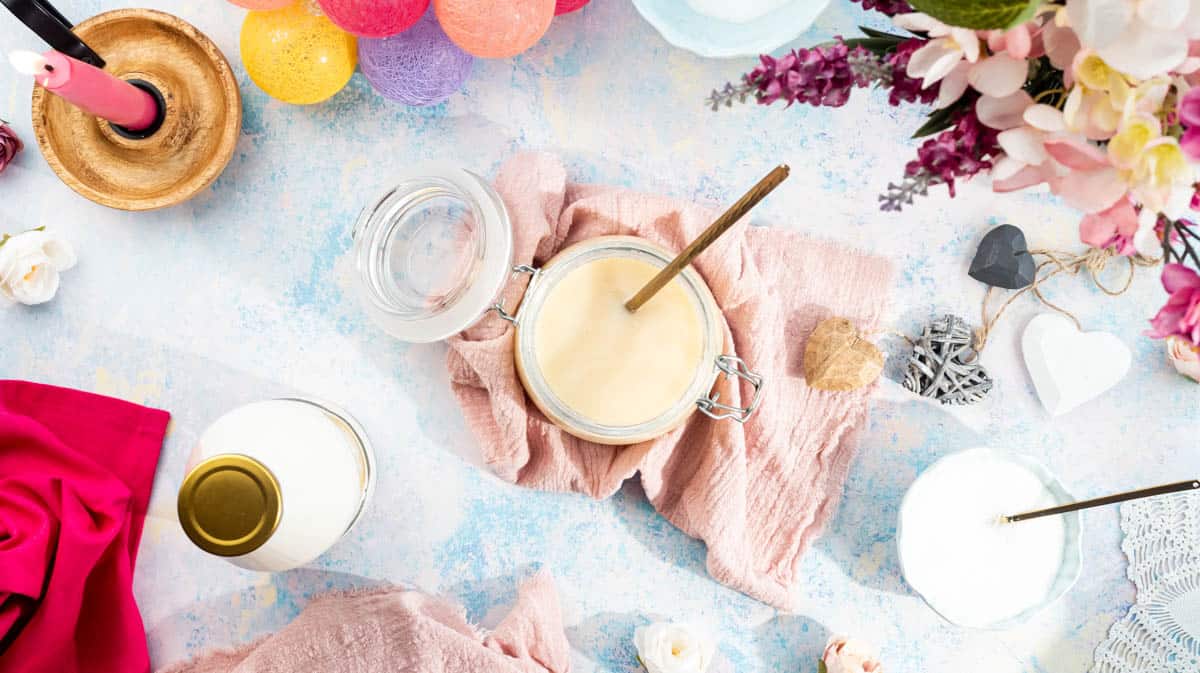A jar of condensed milk with a gold spoon inside surrounded by decorative pink themed items.