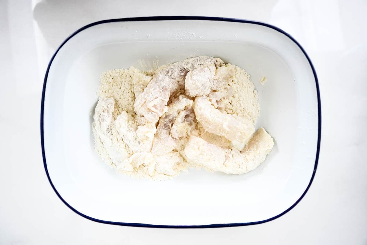 The cut cod pieces inside a shallow dish being coated in flour.