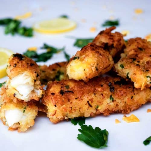 A stack of fish fingers surrounded by fresh herbs and lemon slices.