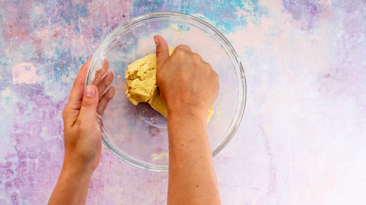 A hand is kneading the pastry dough to form it into a ball.