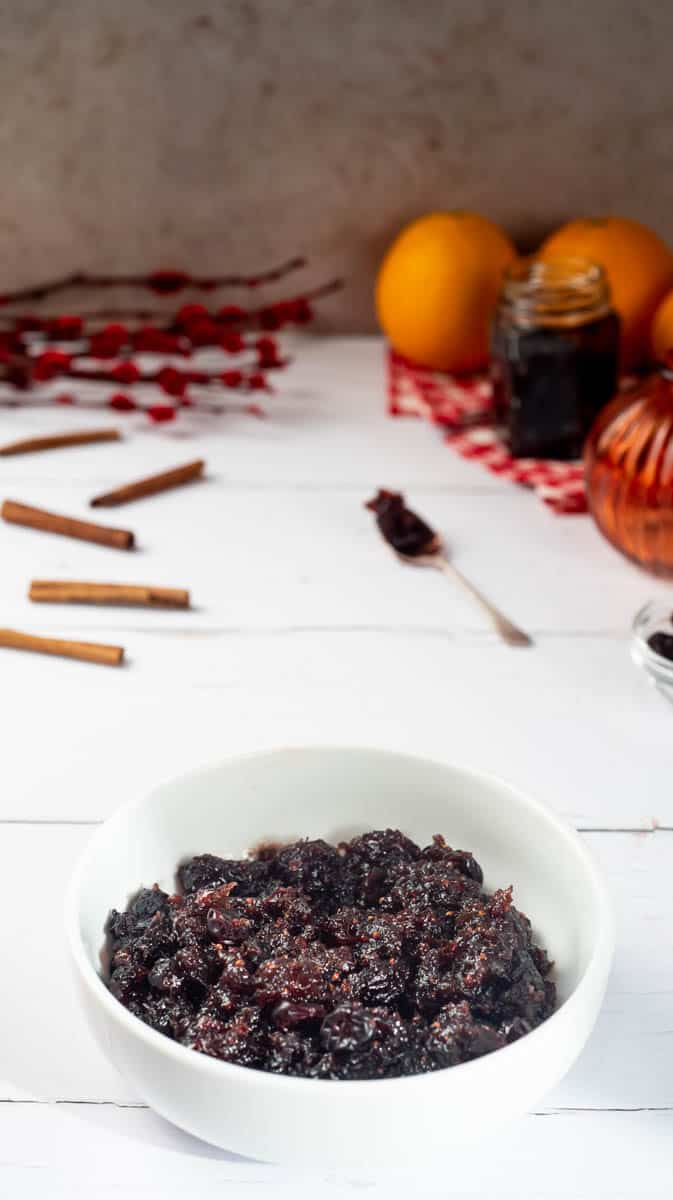 A front view of the cranberry sauce in a white bowl with decorative items in the background.