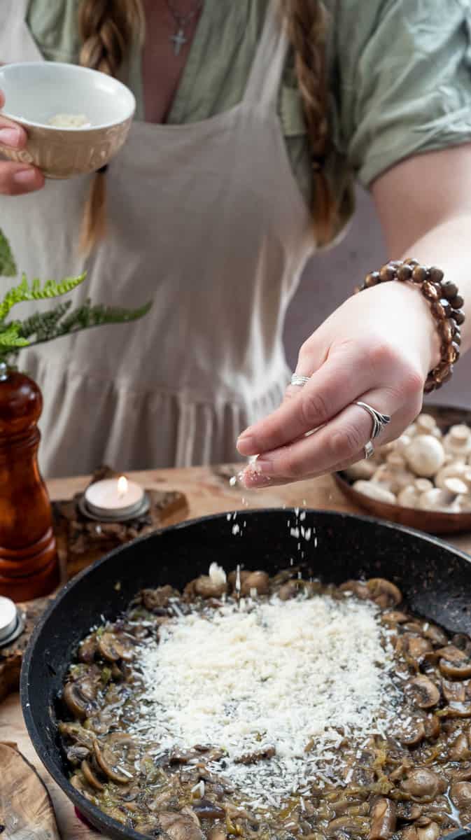 A person is sprinkling parmesan cheese into the sauce for the creamy chicken drumsticks.