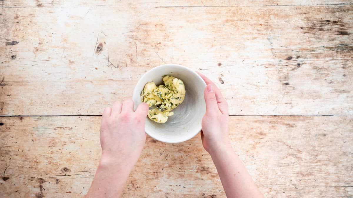 A hand is mixing the sage butter mixture inside a white bowl.