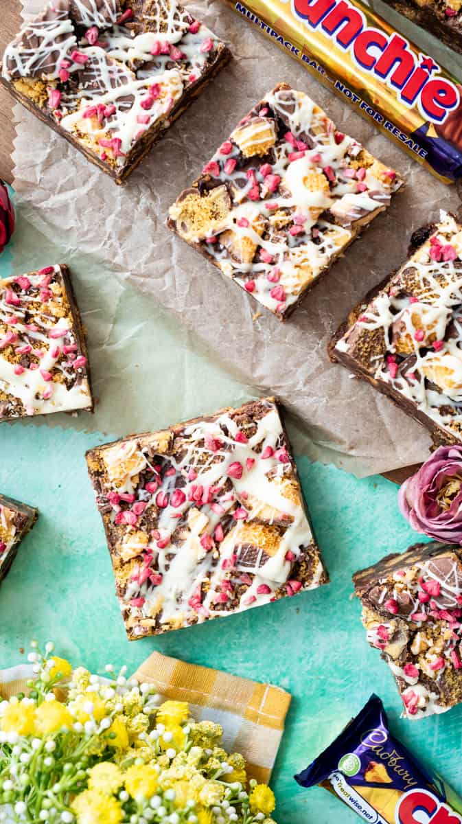 An overhead view of Crunchie Tiffin arranged in a random pattern. With yellow flowers and Crunchie bars as decorations.