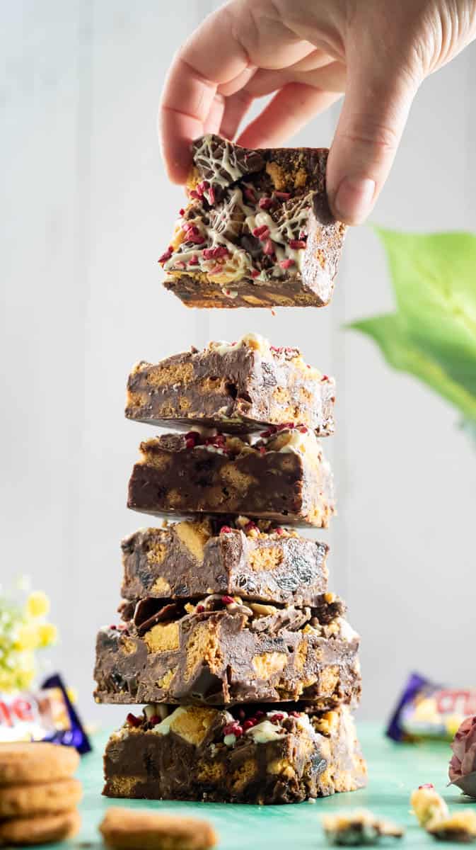 A hand is lifting a Crunchie Tiffin bar from the top of a stack of them.