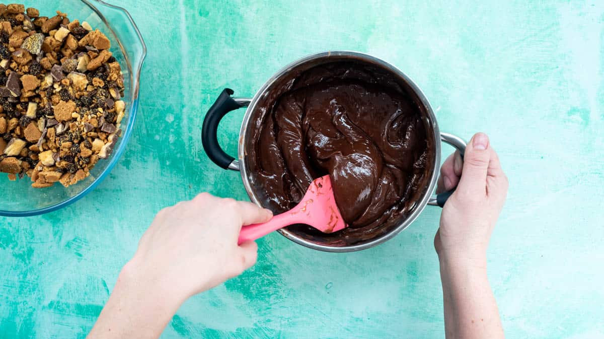 A hand is using a pink spatula to mix the melted chocolate ingredients together.