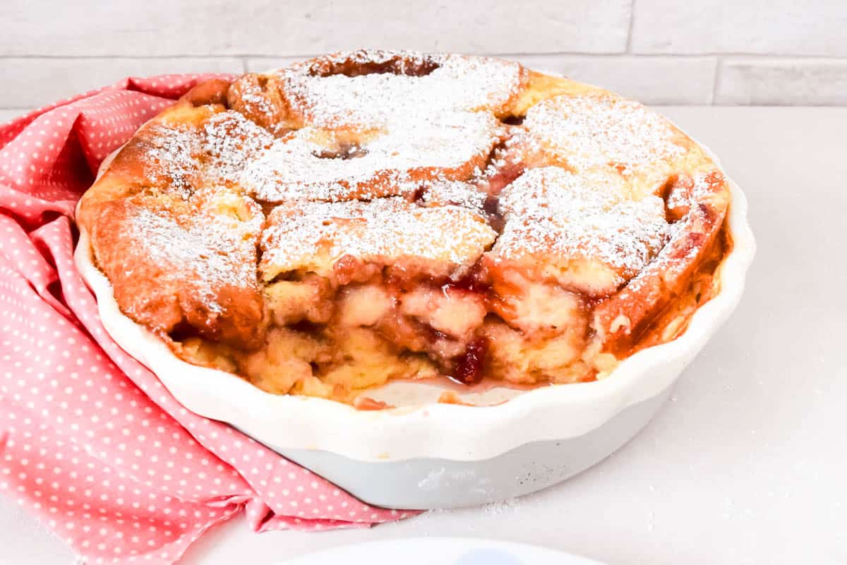 Doughnut bread and butter pudding in a dish with a portion removed to show the layers.