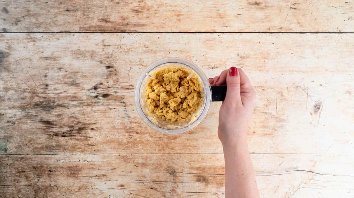 A hand is holding a blender cup filled with blended chickpeas.