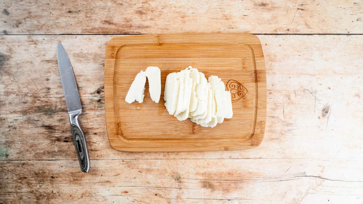 Sliced halloumi on a wooden board with a silver knife to the left.