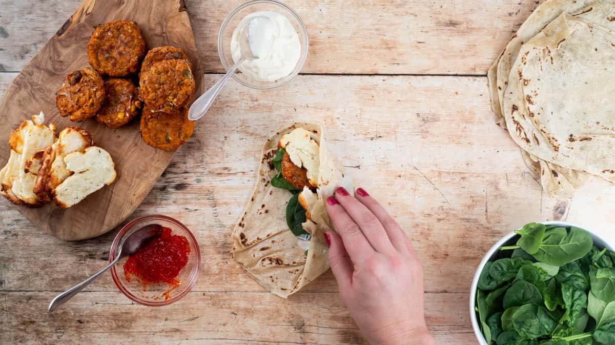 A hand is folding over one side of the falafel and halloumi wrap to demonstrate how to fold the wrap correctly.