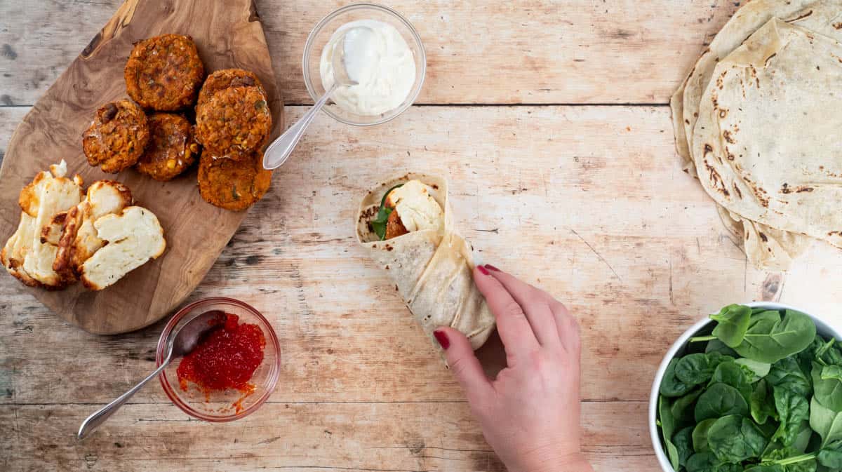 A hand is folding the final side of the wrap to encase the filling ingredients and keep everything inside.