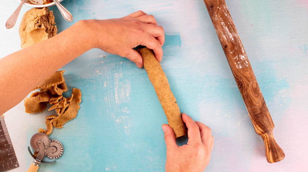 Two hands are completing the rolling up to encase the fig filling in the dough.