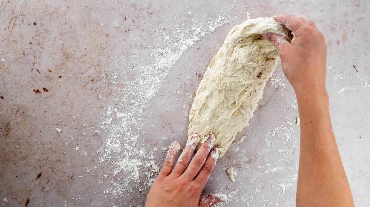 Two hands are beginning to knead the dough on a floured surface.