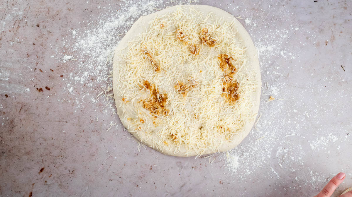 A round dough disc covered in roasted garlic and grated parmesan cheese.