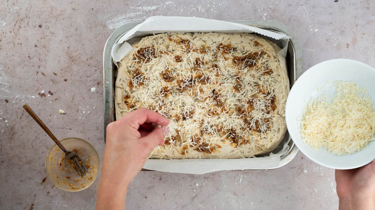A hand is sprinkling parmesan cheese on top of the dough inside the tin.
