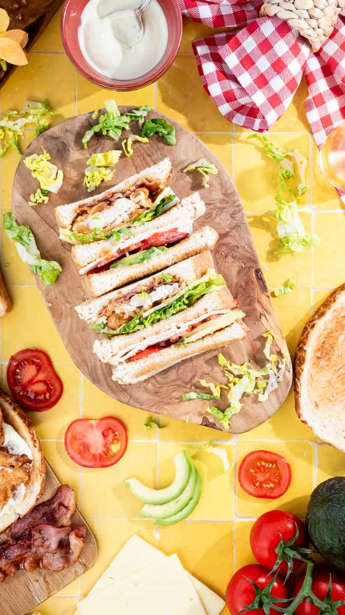 A fried chicken club sandwich sliced and laid face up towards the camera on a wooden board.