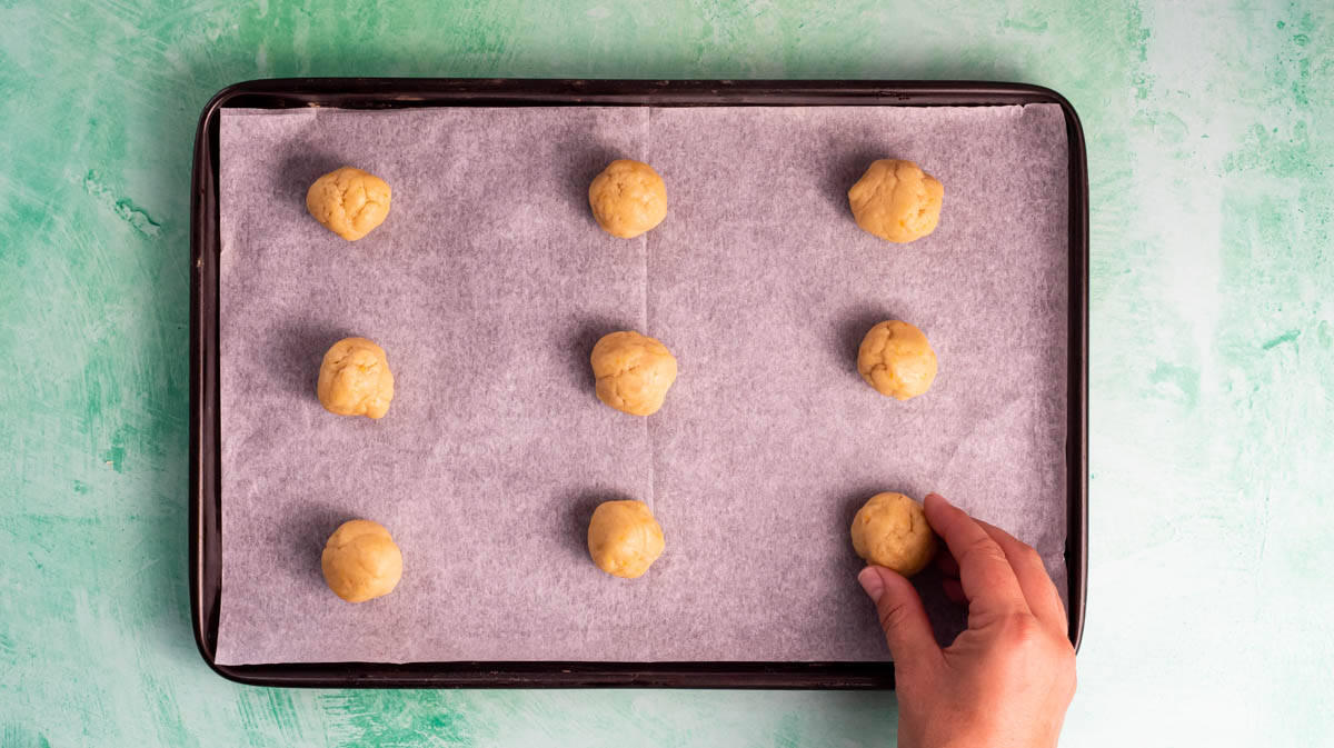A hand is placing small balls of dough onto a lined baking tray.