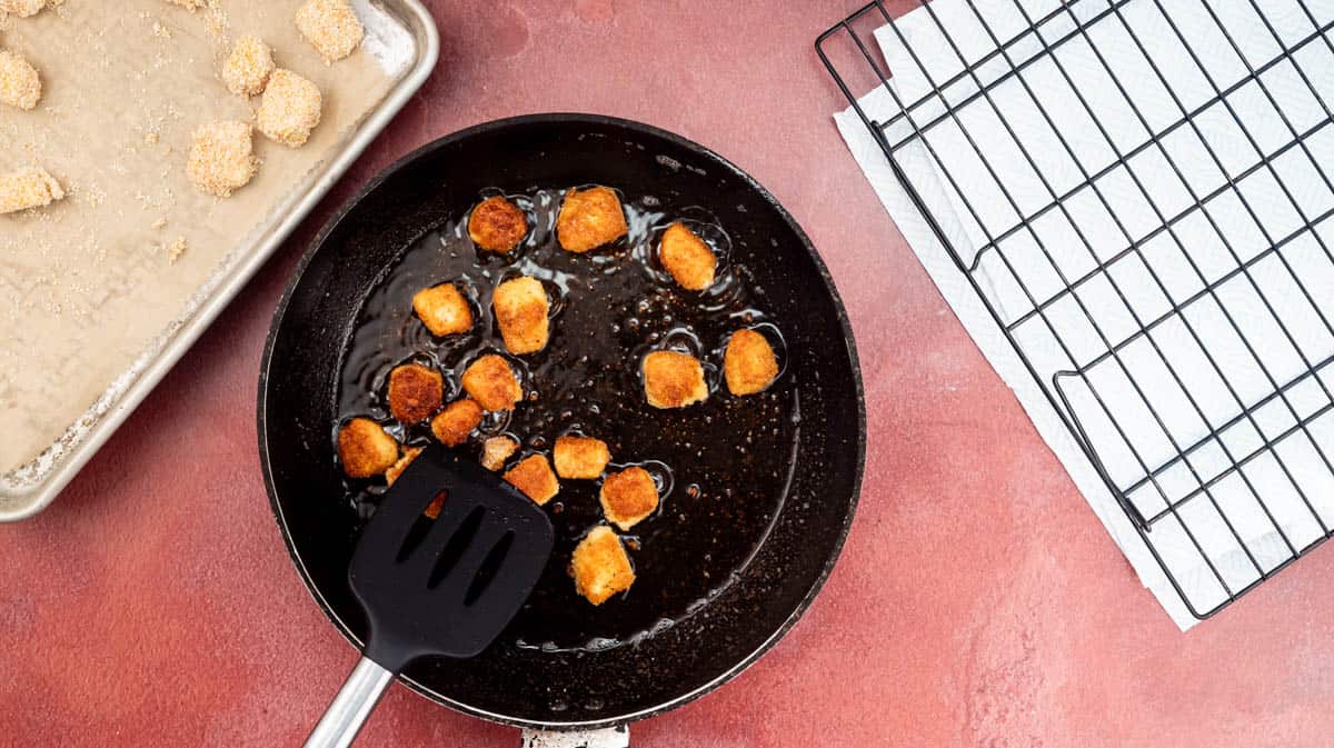 A black frying pan with golden brown halloumi nuggets frying inside.