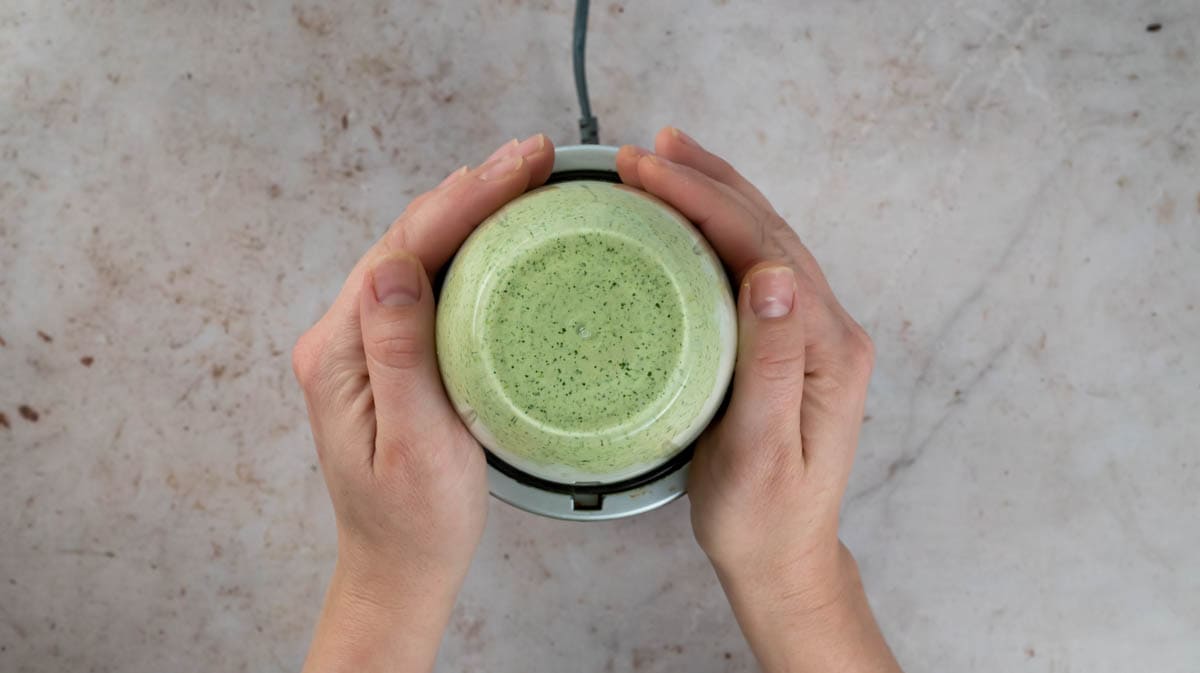 Two hands are cupping a blender while the jalapeno mayo ingredients are blending together inside.