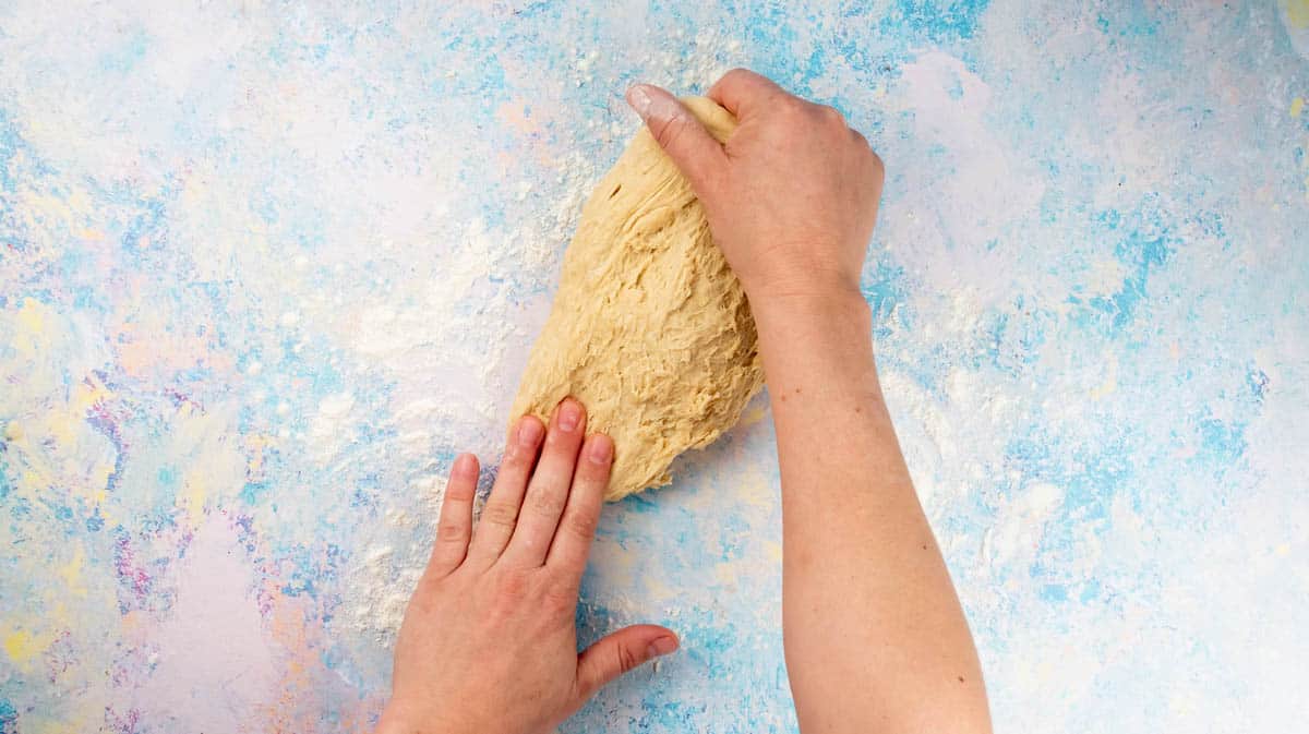 Two hands are kneading dough on a floured surface.