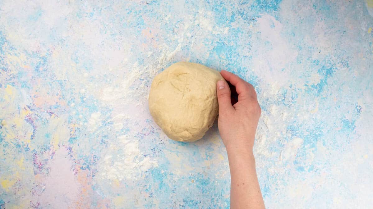 A hand has shaped the kneaded dough into a ball.