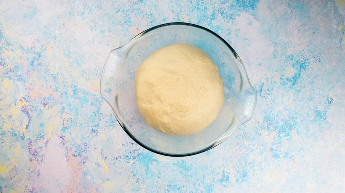 A glass bowl with risen doughnut dough inside.