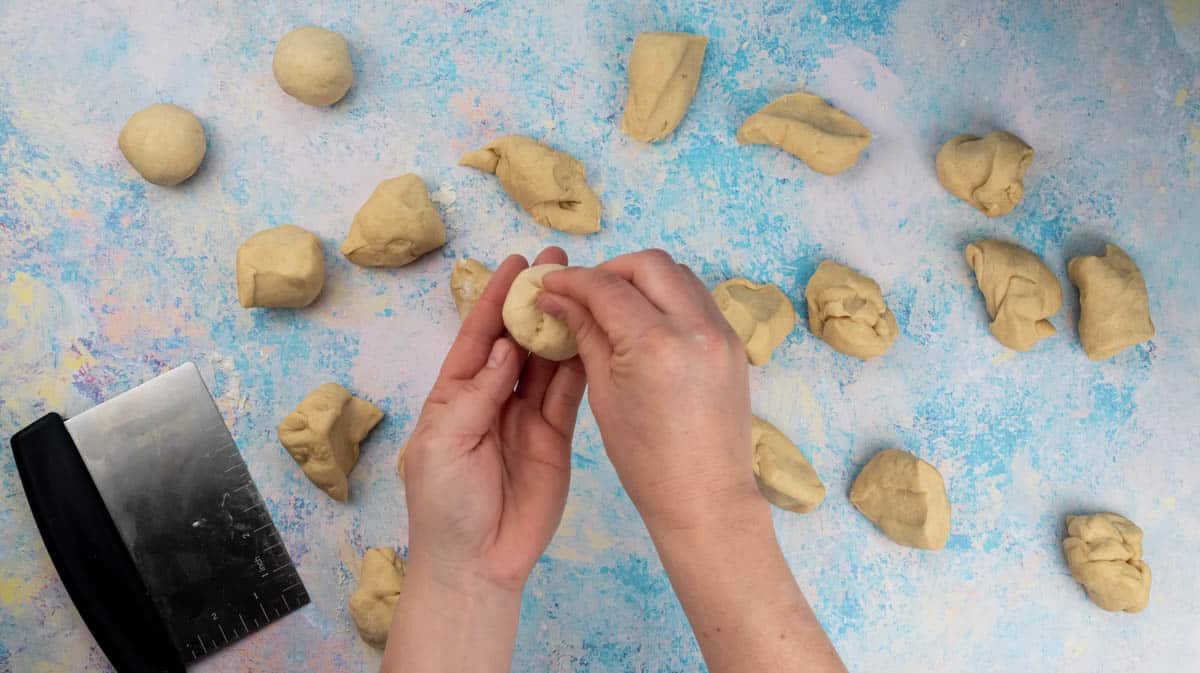 A hand is pinching the bottom of a doughball to seal it.