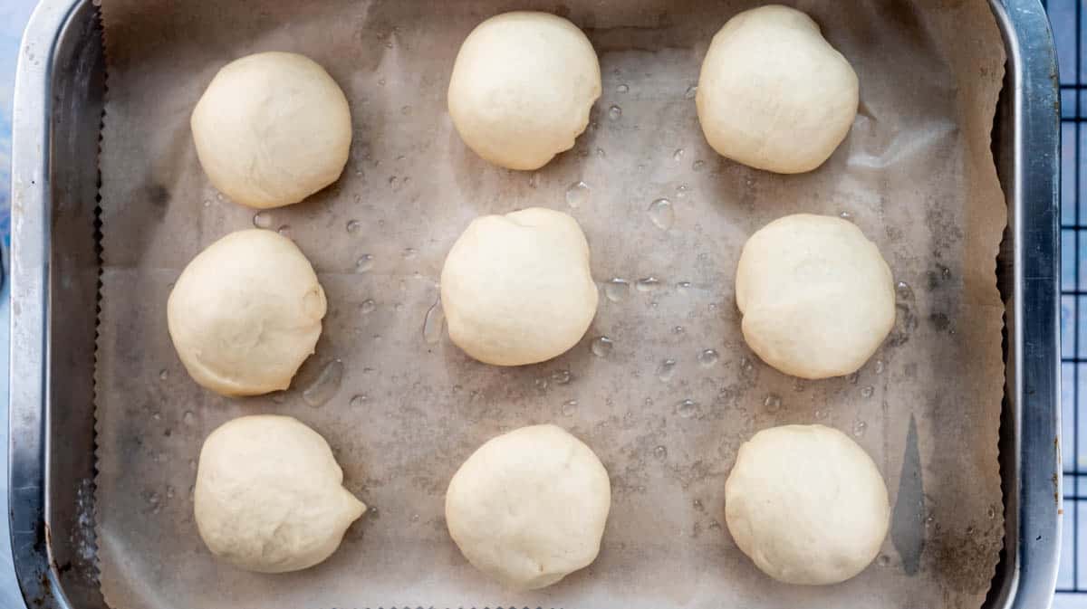 Risen doughballs inside a lined baking tray.