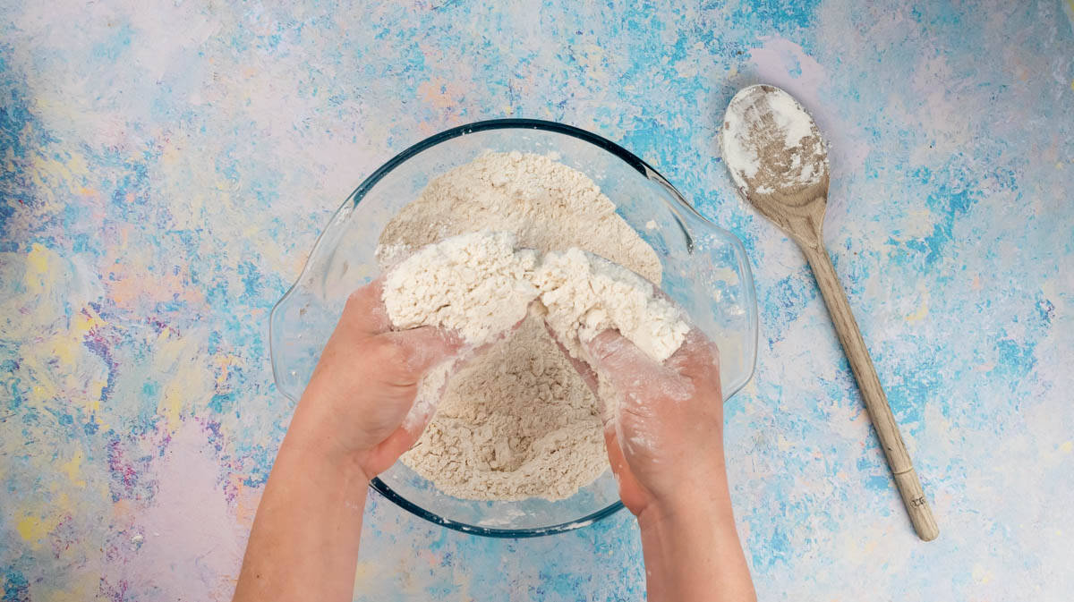 Two hands are rubbing butter into flour to create a breadcrumb texture.