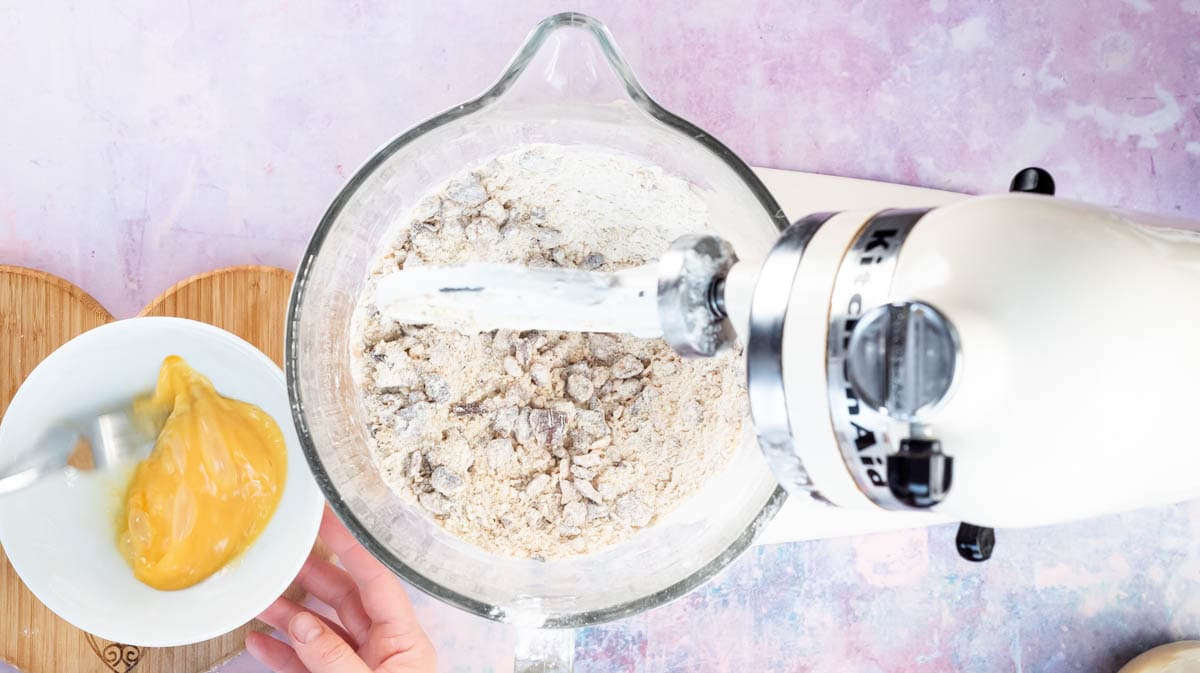 A hand is using a fork to whisk eggs in a bowl next to a stand mixer.
